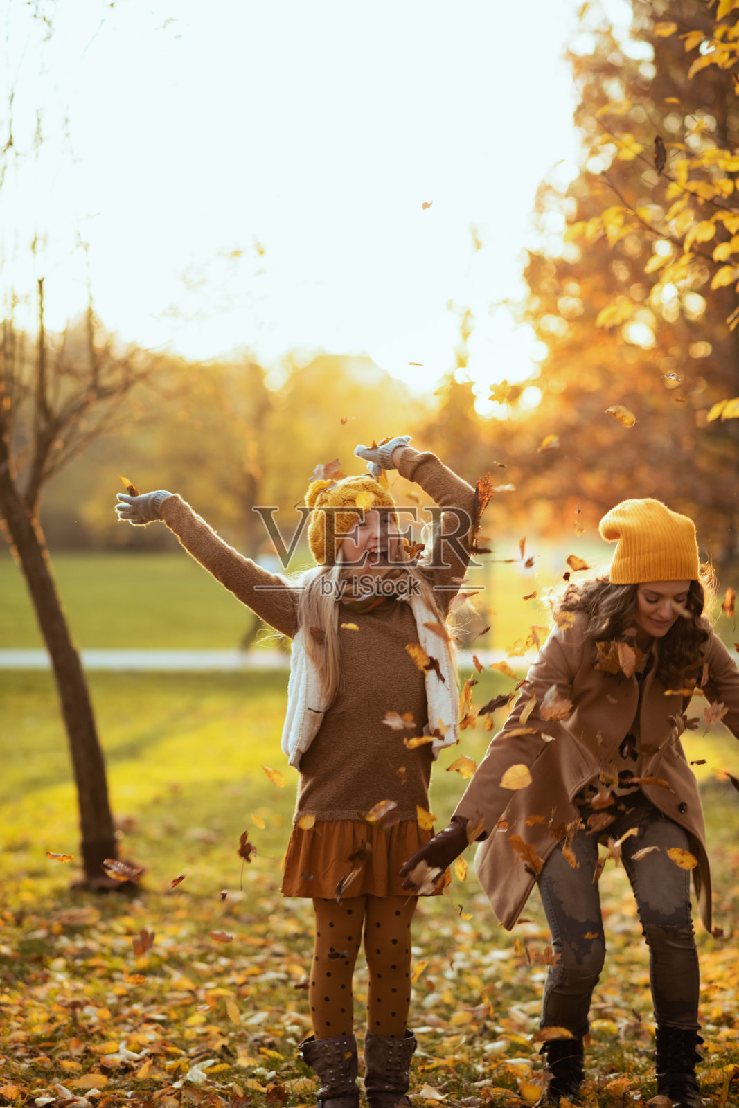 年轻的母亲和孩子微笑着扬起秋叶照片摄影图片