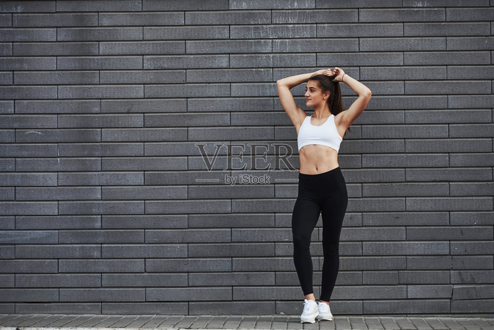年轻的运动的深色头发和苗条的身材在城市的砖墙在白天照片摄影图片