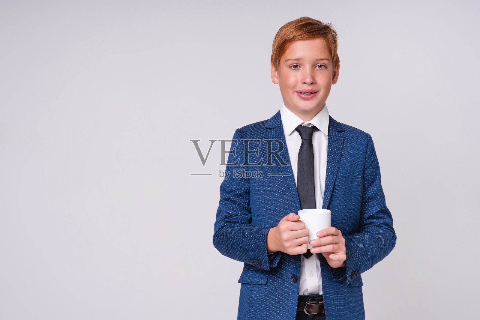 可爱的红发男孩穿着正式的衣服拿着一杯咖啡孤立在灰色的背景照片摄影图片