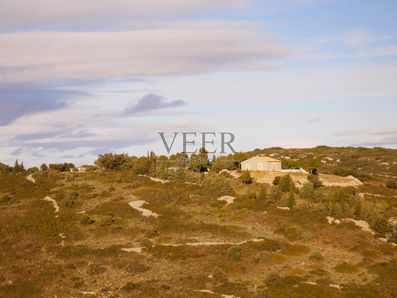 日落时被树木环绕的小山上的乡村房屋照片摄影图片