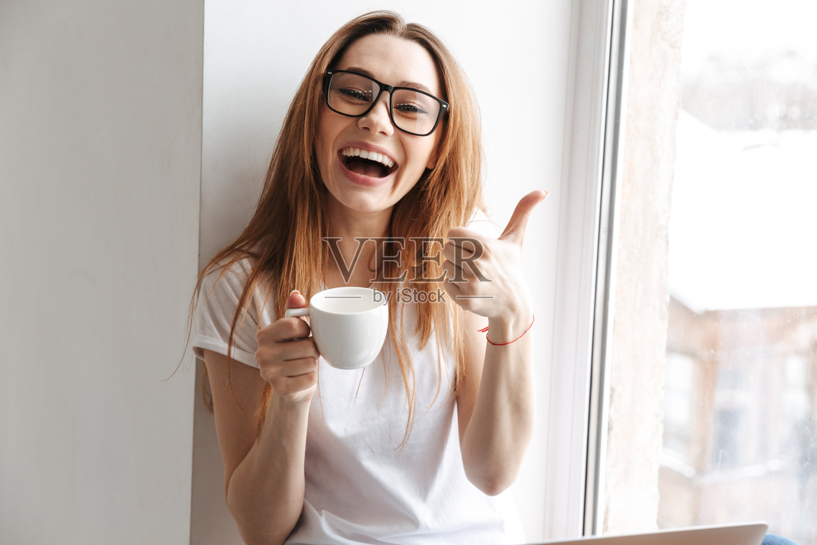 穿着t恤,戴着眼镜的快乐女人坐在窗台上照片摄影图片