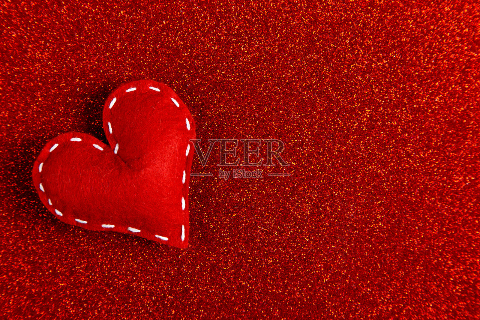 手工缝制柔软的感觉心在红色闪亮的背景,亮片在一边。情人节的概念。副本的空间。照片摄影图片