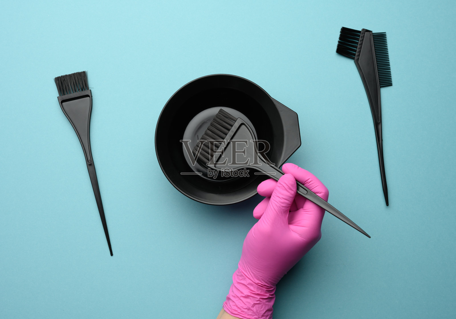 蓝色背景上,一只手戴着粉色橡胶手套的女性手上拿着用来染头发的塑料配件照片摄影图片