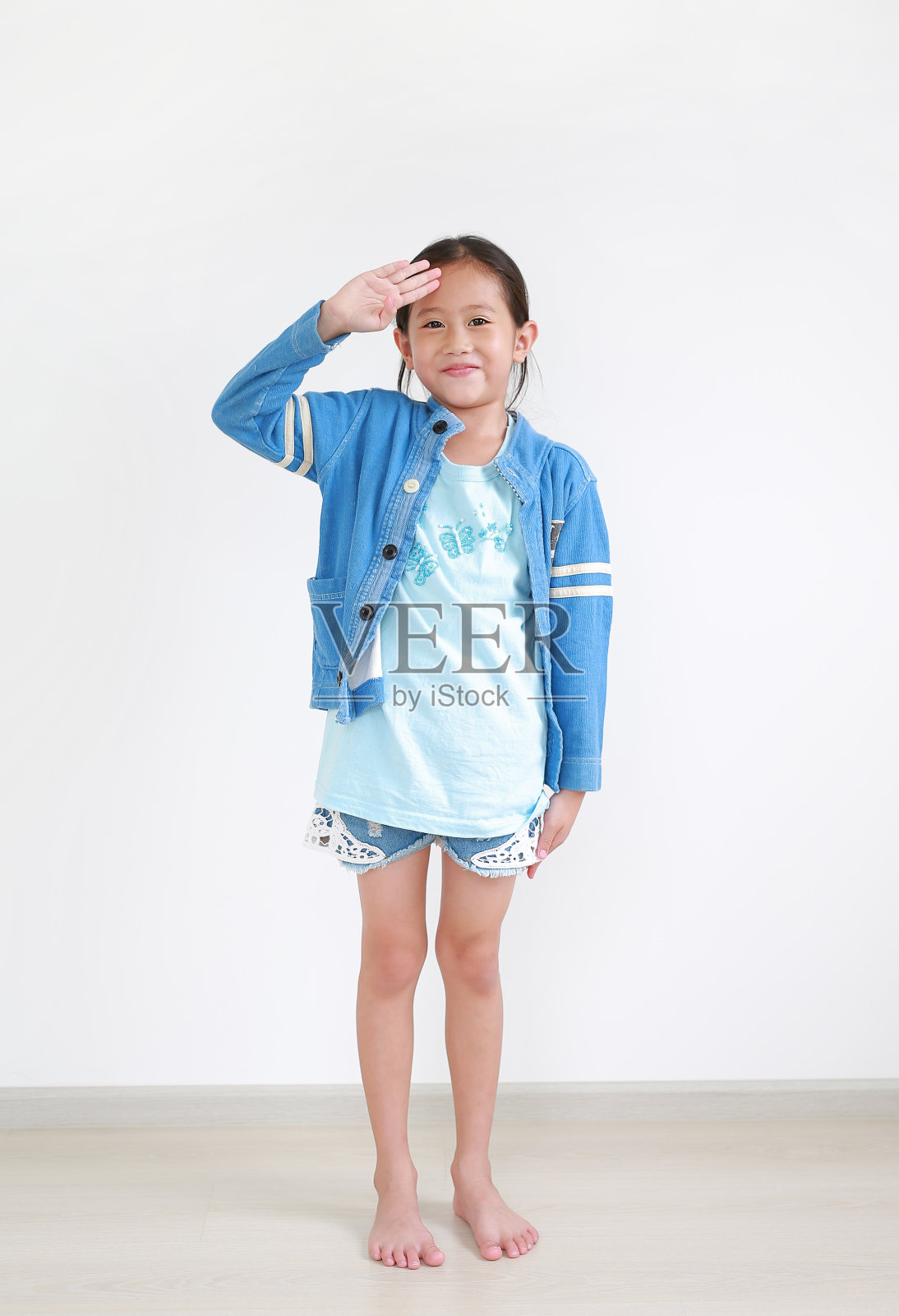 亚洲小女孩的肖像与手在前额室内敬礼。全身。照片摄影图片