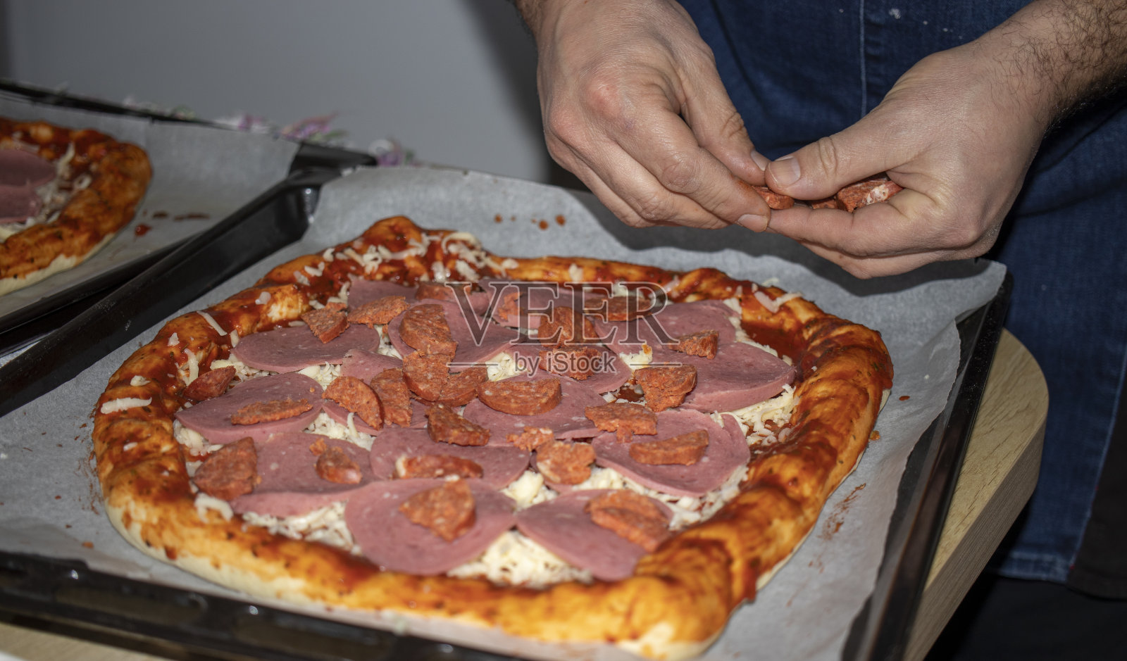 在自家厨房里准备披萨的男人。他将馅料依次排列在披萨面团上。照片摄影图片