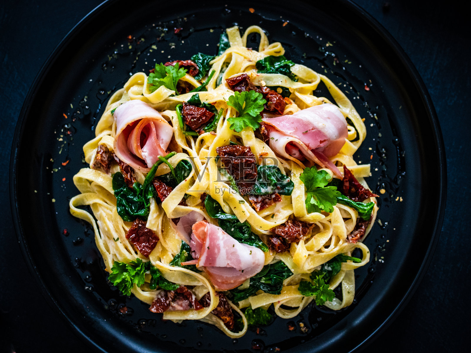 黑色的桌子上放着菠菜,培根,晒干的番茄和阿尔弗雷多酱照片摄影图片