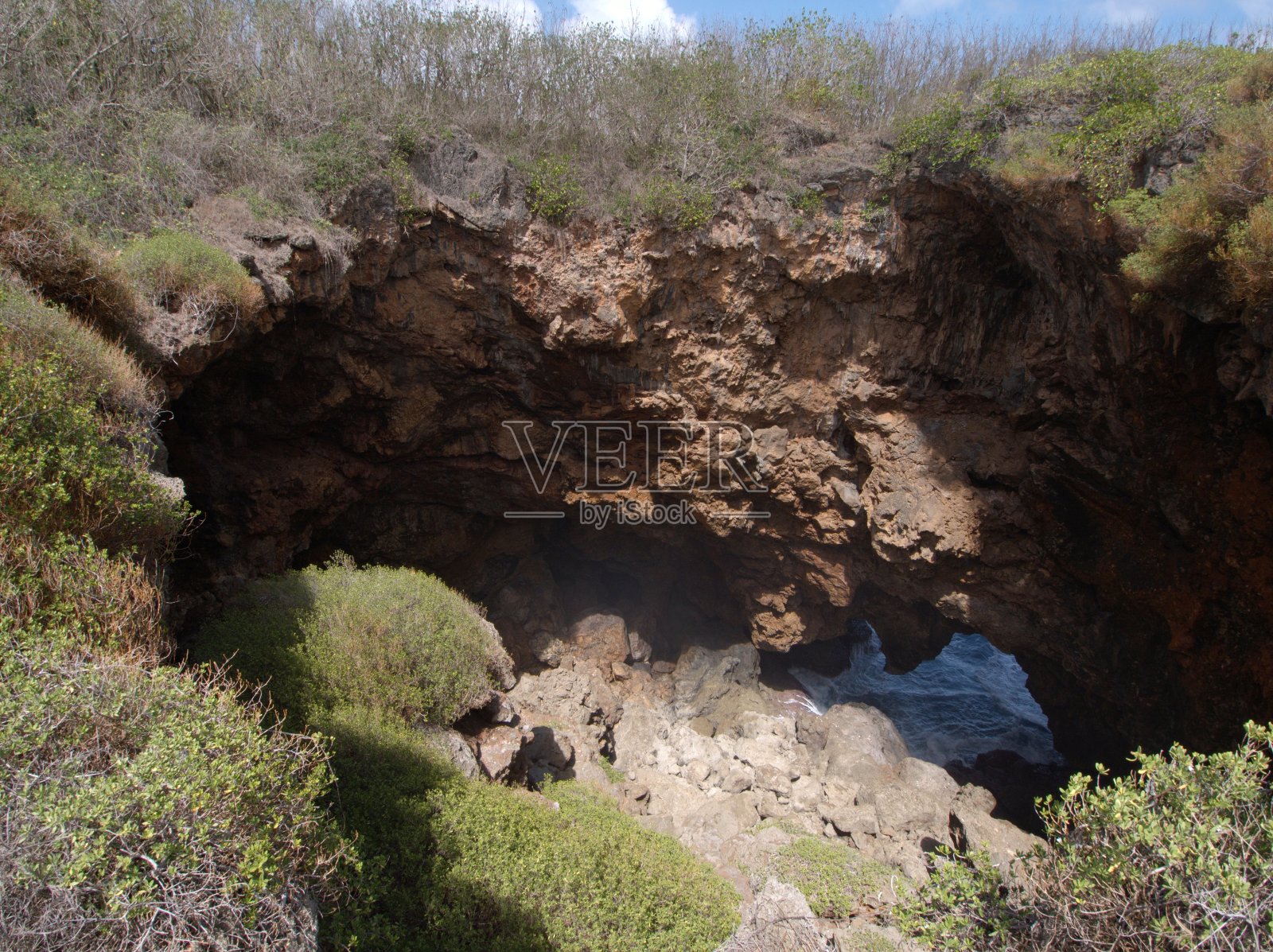 悬崖上的深渊俯瞰着一个巨大的洞,里面有锋利的岩石和海水照片摄影图片