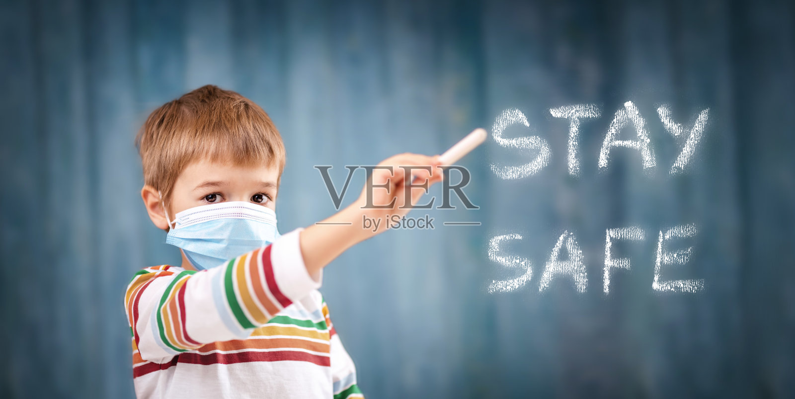 男孩在医疗脸保护面具室内在蓝色背景。照片摄影图片