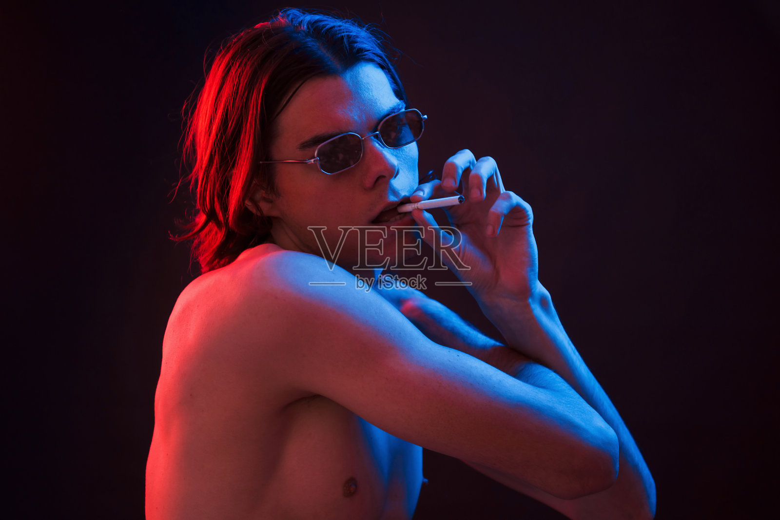 拿着香烟。工作室拍摄在黑暗的工作室与霓虹灯。严肃男人的肖像照片摄影图片