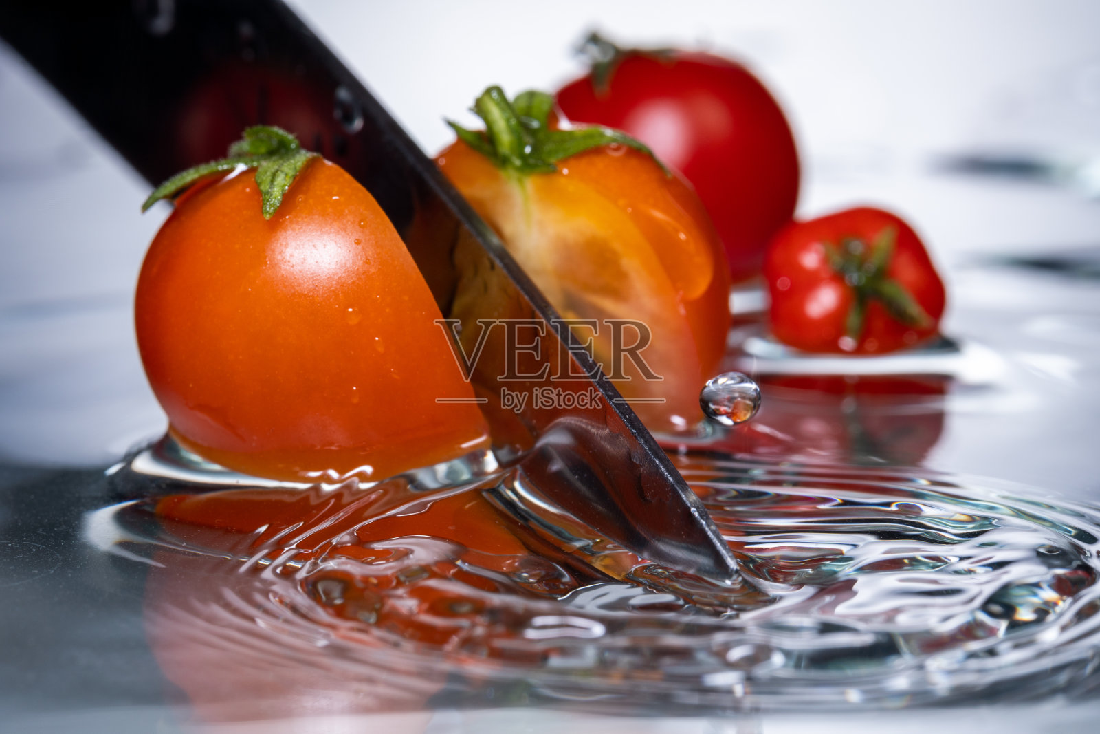 小红的樱桃番茄用刀切,在水中随水珠滴下,冻结运动照片摄影图片