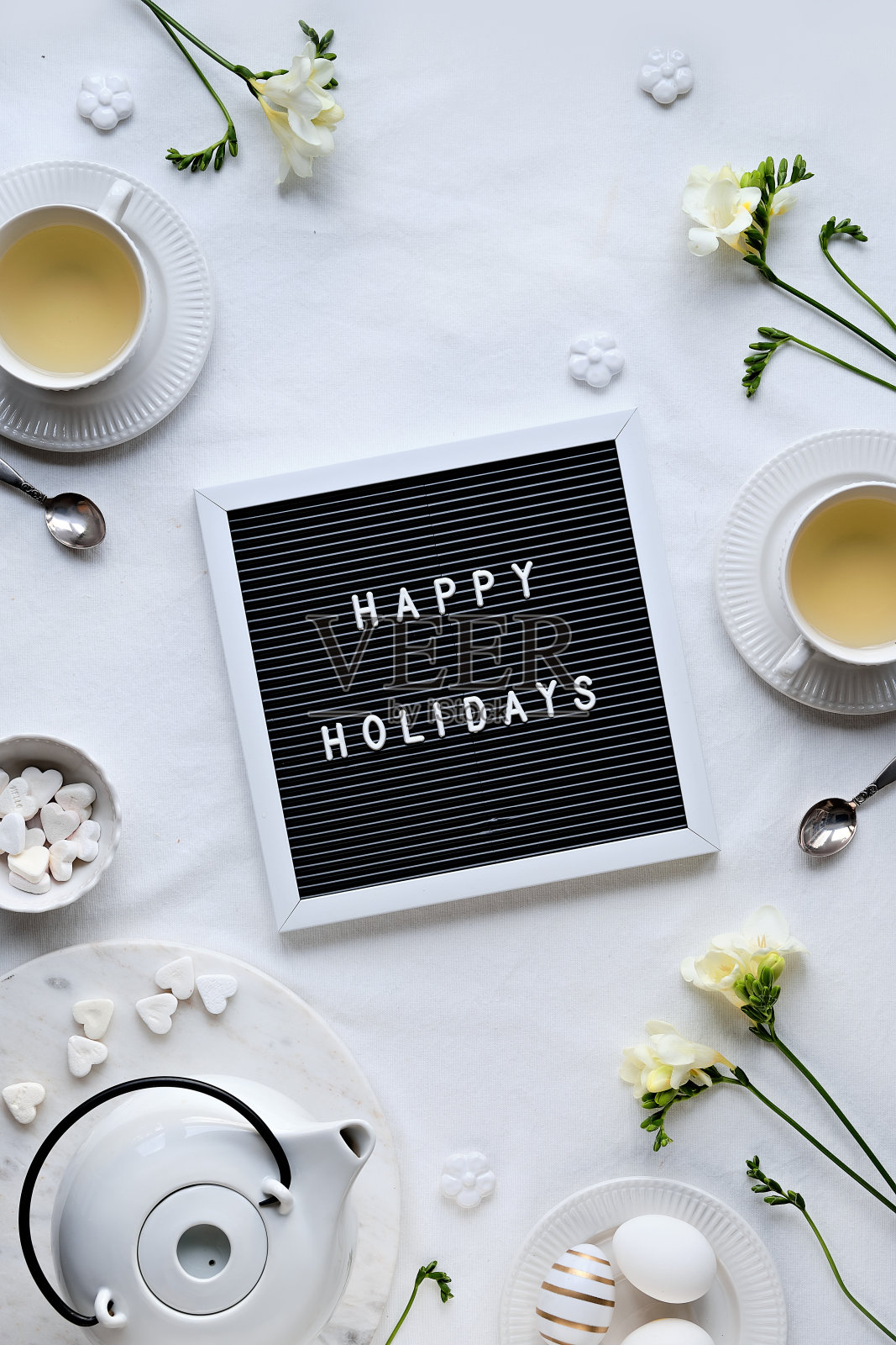 在写字板上写上节日快乐,桌上放着春天的小苍兰花和茶杯。黑色letterboard。复活节彩蛋,白色陶瓷杯和糖心。平铺,象牙纺织品桌布照片摄影图片