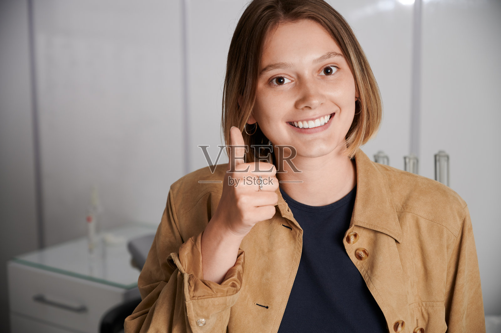 美丽的黑发女子在牙医诊所给大拇指。照片摄影图片