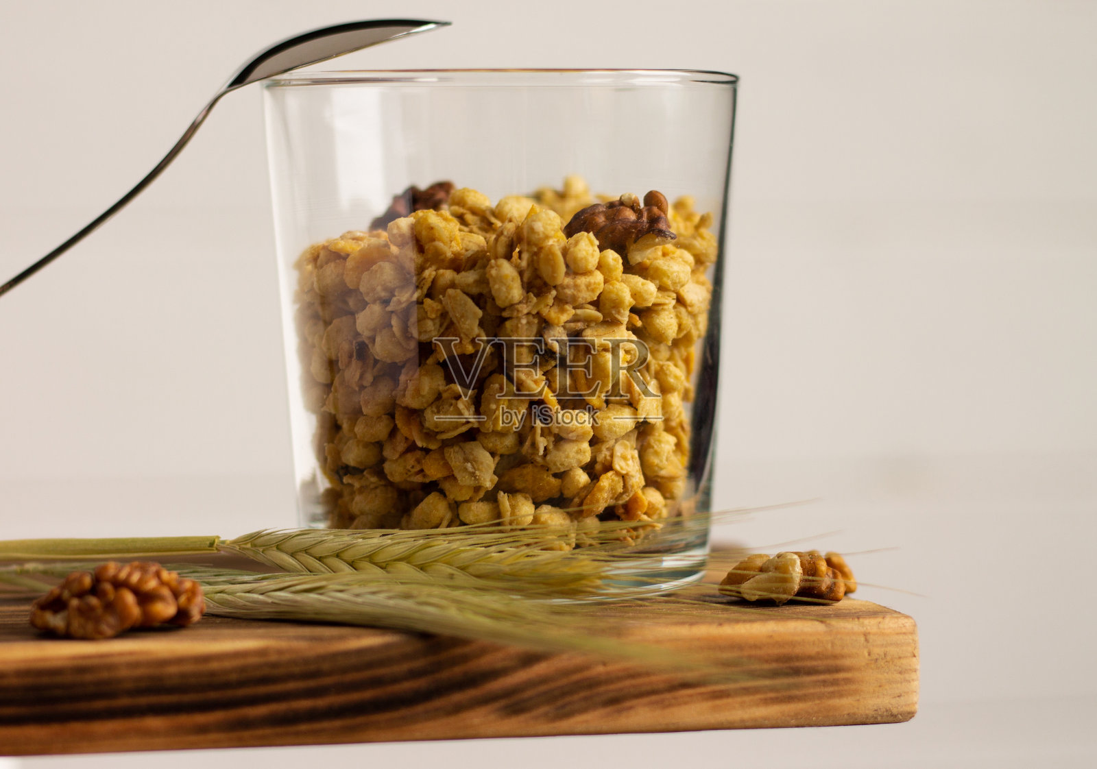 麦片麦片在一个透明的玻璃与黑麦穗,勺子和核桃架子上的白色背景。照片摄影图片