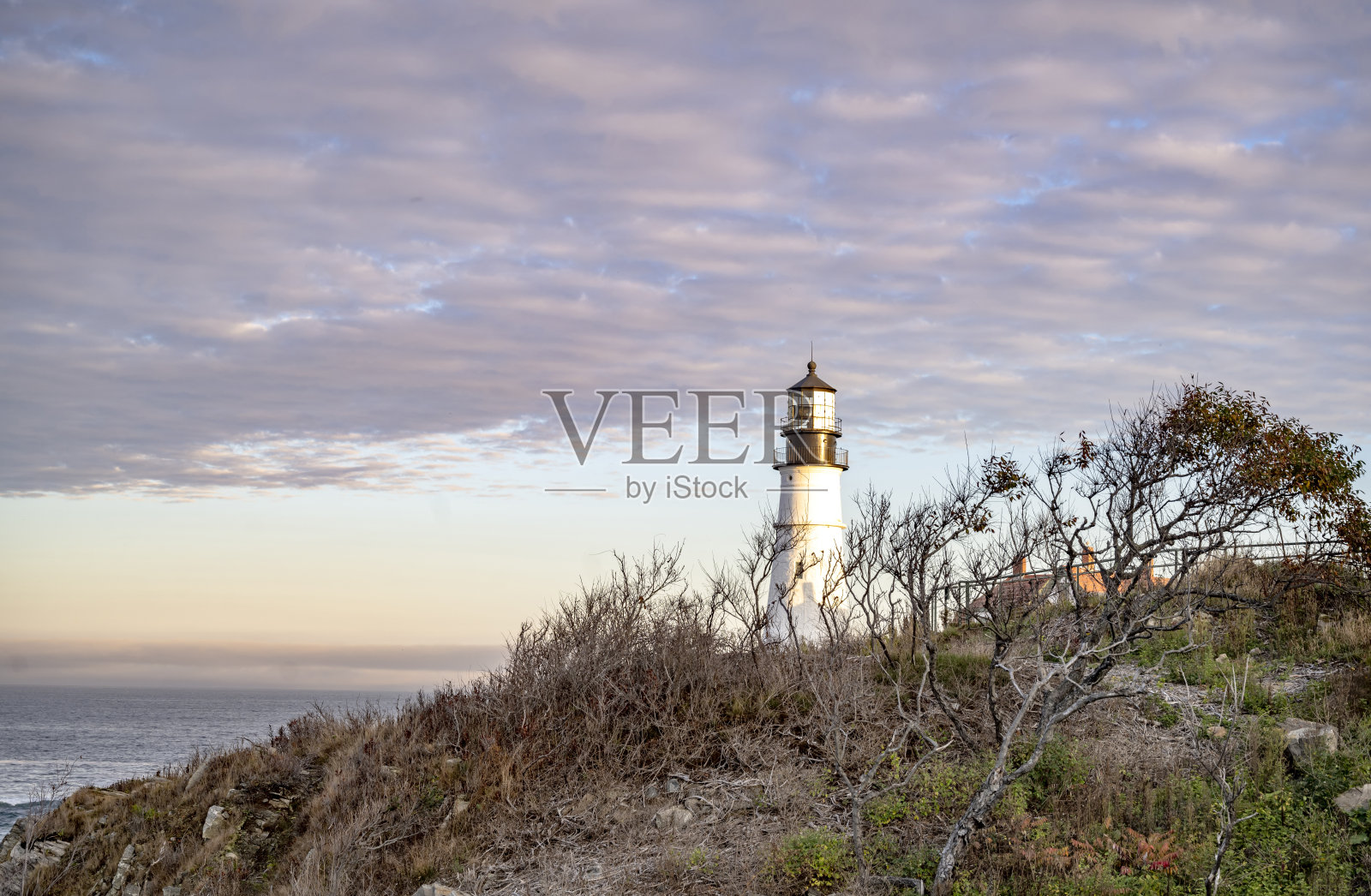 在新英格兰缅因州波特兰市大西洋沿岸多云的天空下,一座茂密的悬崖顶上的灯塔正在工作照片摄影图片
