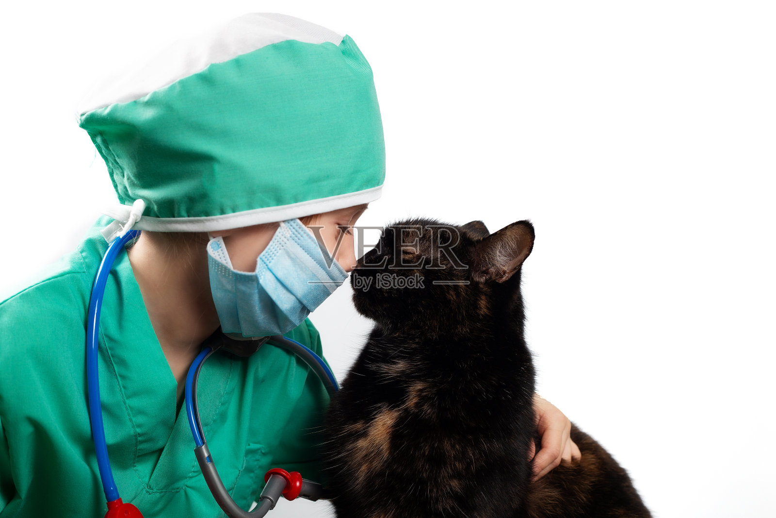 身着绿色外科手术服,戴着医用防护面具的女孩与家养黑猫玩起了兽医的游戏照片摄影图片