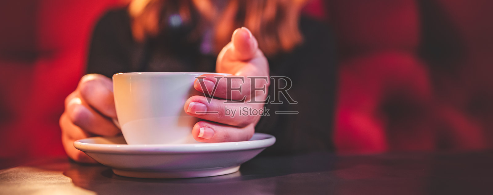 女人手拿着一杯白色的茶或咖啡站在咖啡馆的桌子上照片摄影图片