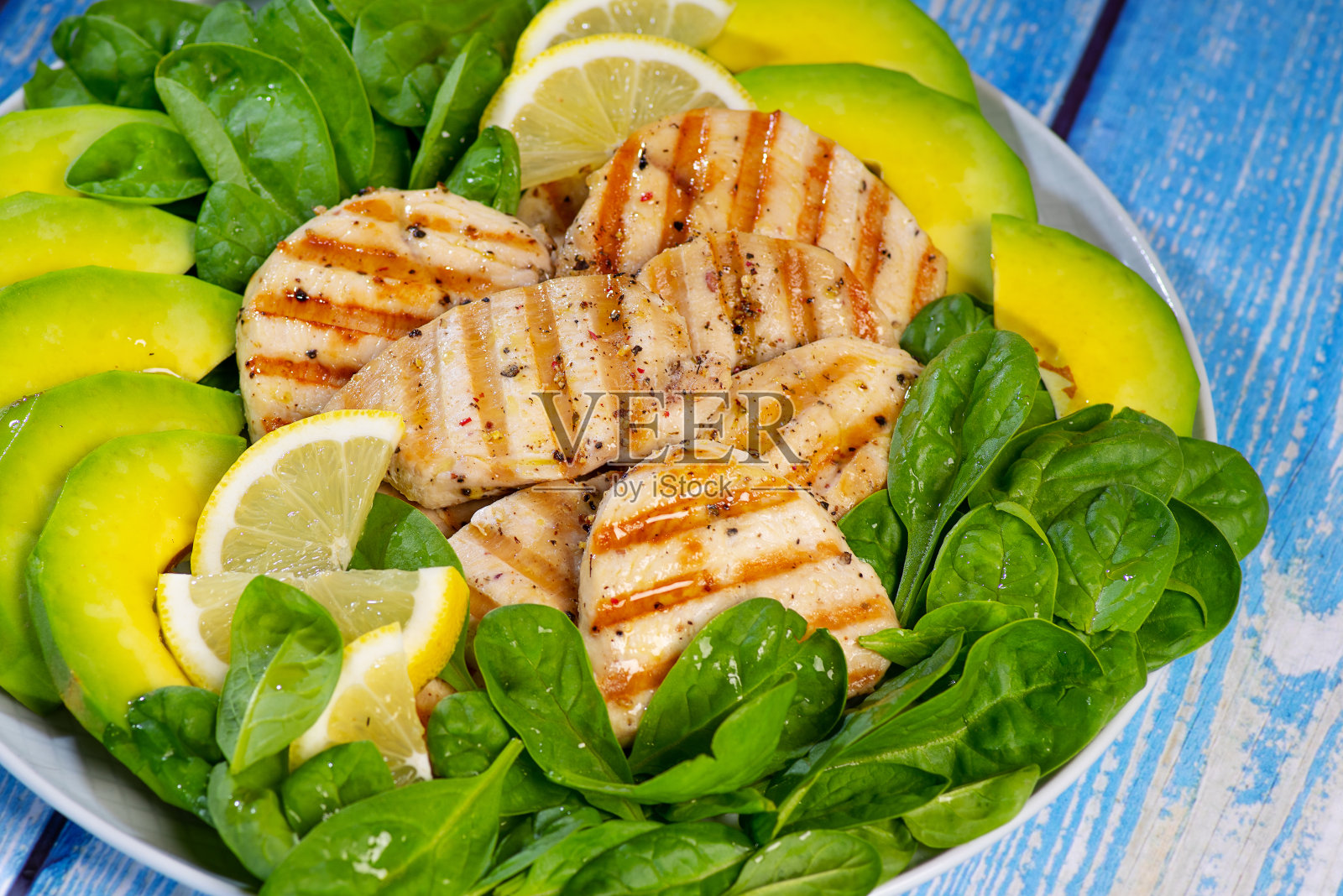 健康鸡佛碗配蔬菜。烤鸡柳配柠檬片,菠菜片,鳄梨片和香料。烤鸡沙拉。清洁平衡的健康食品理念。俯视图照片摄影图片