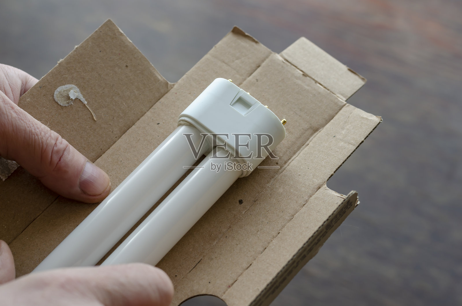 一只手从硬纸板包装里拿出一个新的紧凑型荧光灯。照片摄影图片