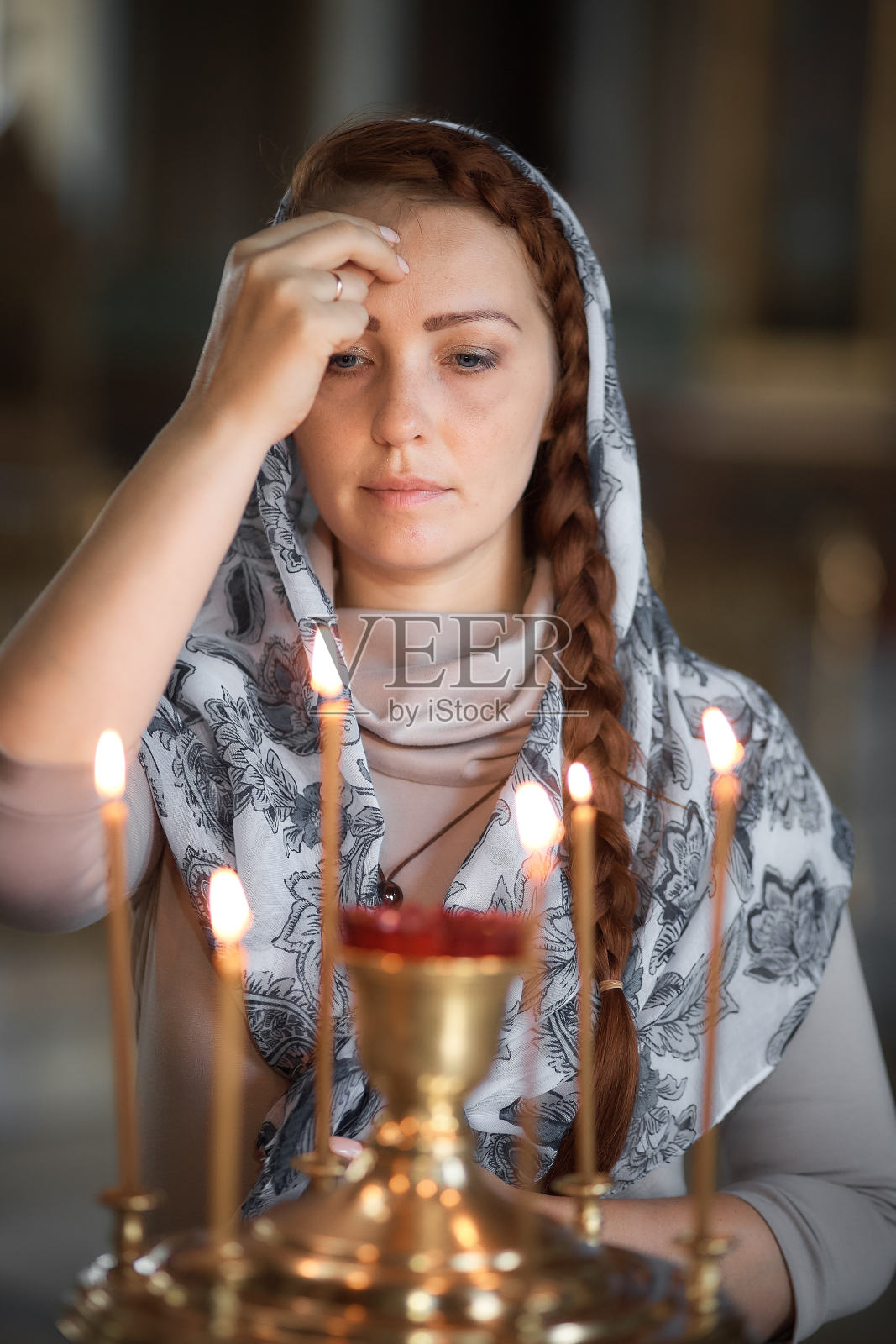 俄罗斯美丽的高加索女人红头发和头巾在她的头上是在东正教,点燃蜡烛和祈祷在圣像前。照片摄影图片