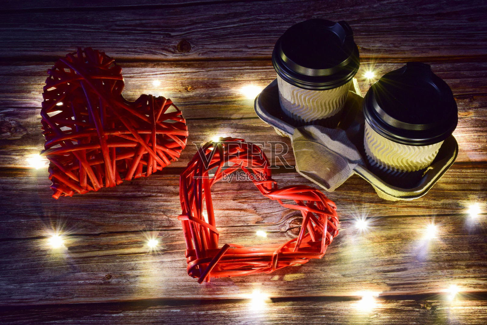 木质背景上,右边是两杯咖啡,左边是两颗装饰性的编织心。发光的光散布在周围照片摄影图片