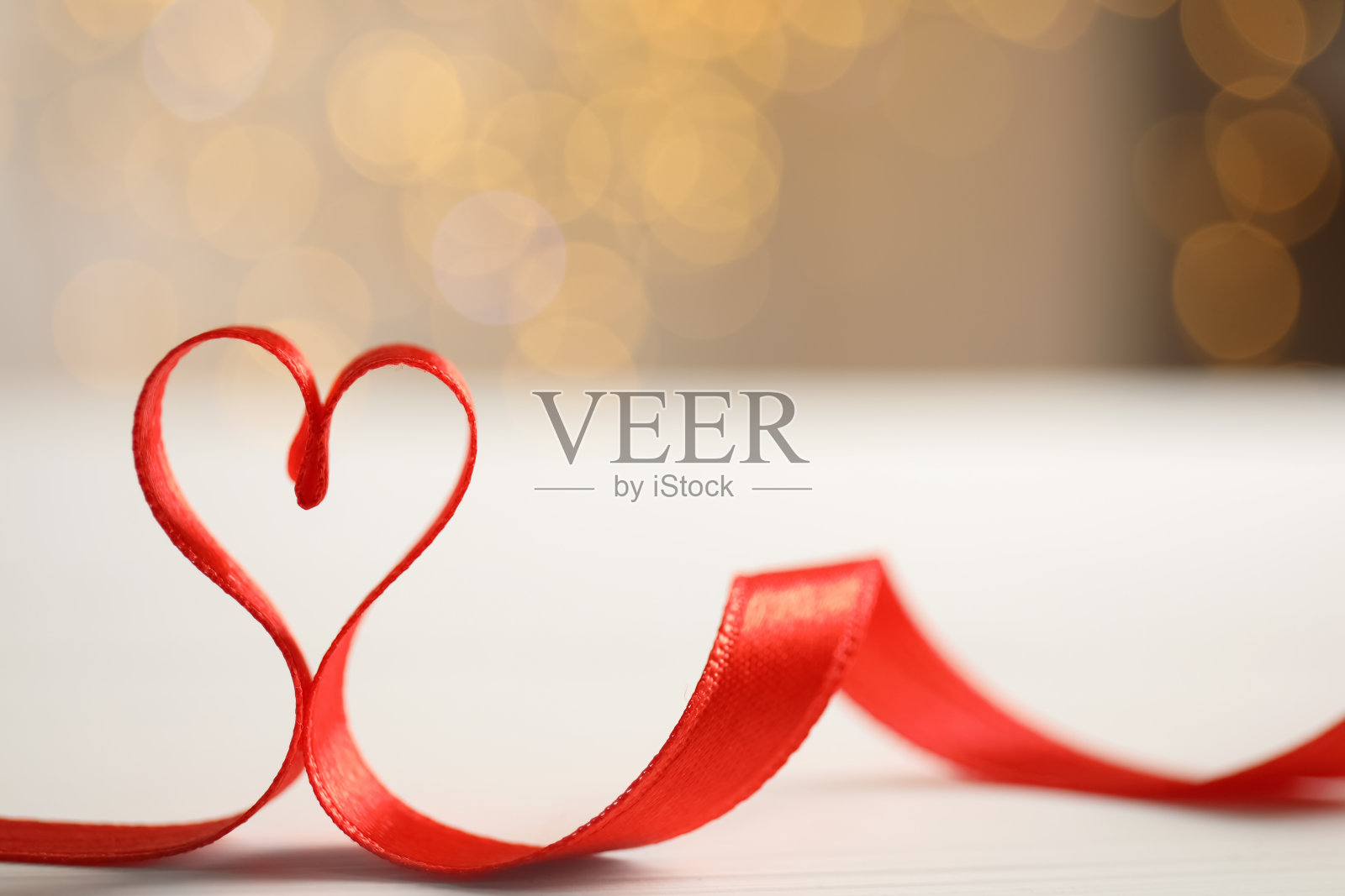 心用红丝带做成的桌子上衬着模糊的节日彩灯,留出文字空间。情人节庆祝活动照片摄影图片