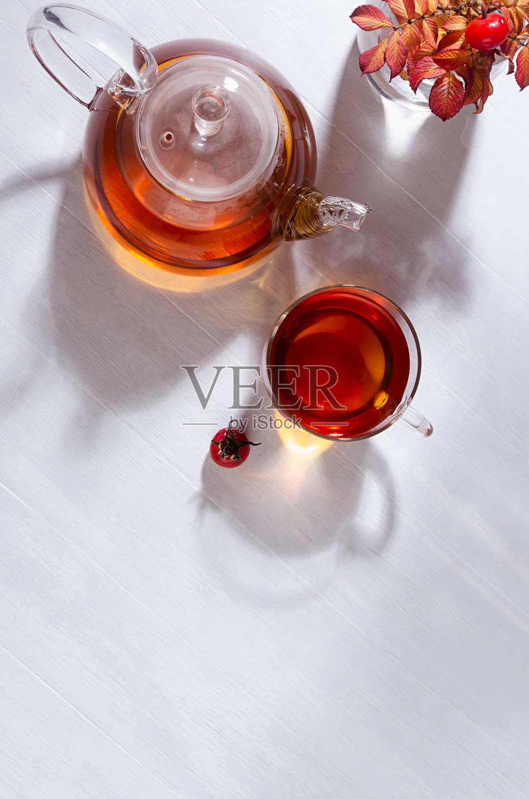 阳光明媚的秋季茶点与玫瑰果茶与茶壶,杯,橙色玫瑰果枝与阴影在白色木桌子上顶视图,复制空间,垂直。照片摄影图片