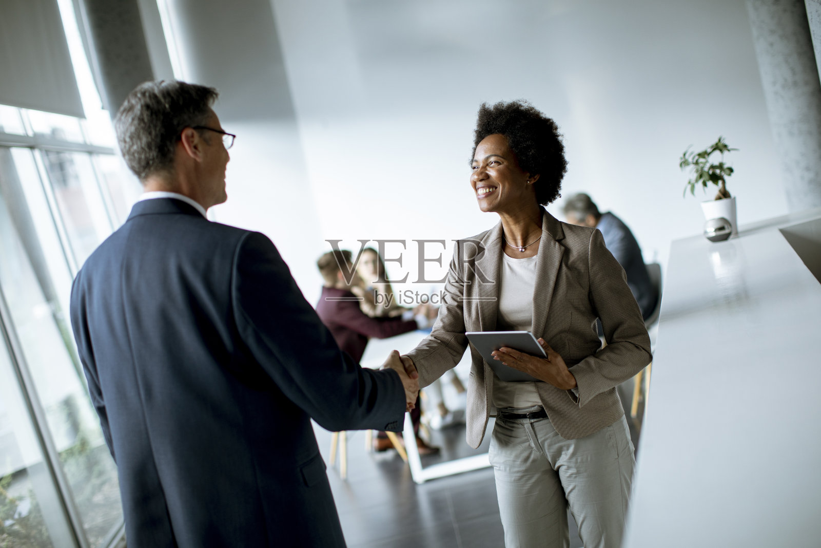 在办公室握手时,女商人拿着平板电脑,看着帅气的同事照片摄影图片