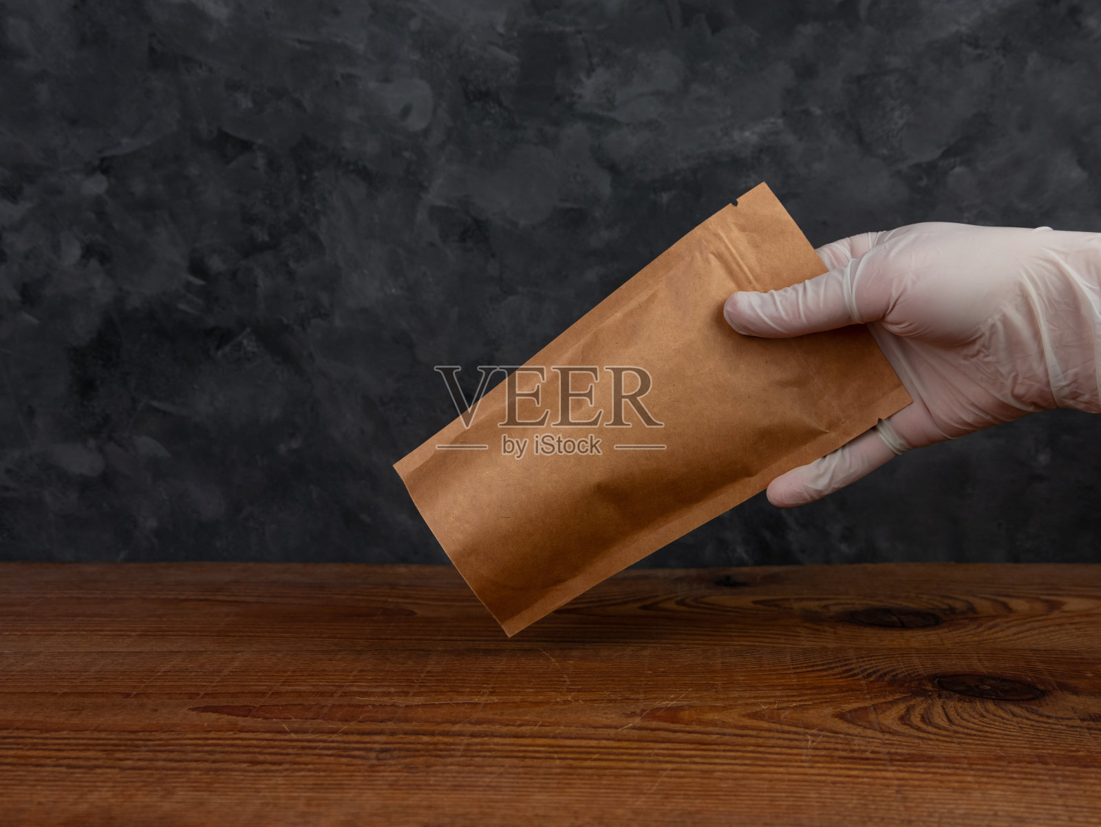 袋袋模型。手握保护手套的棕色牛皮纸包装与咖啡豆木制背景。照片摄影图片