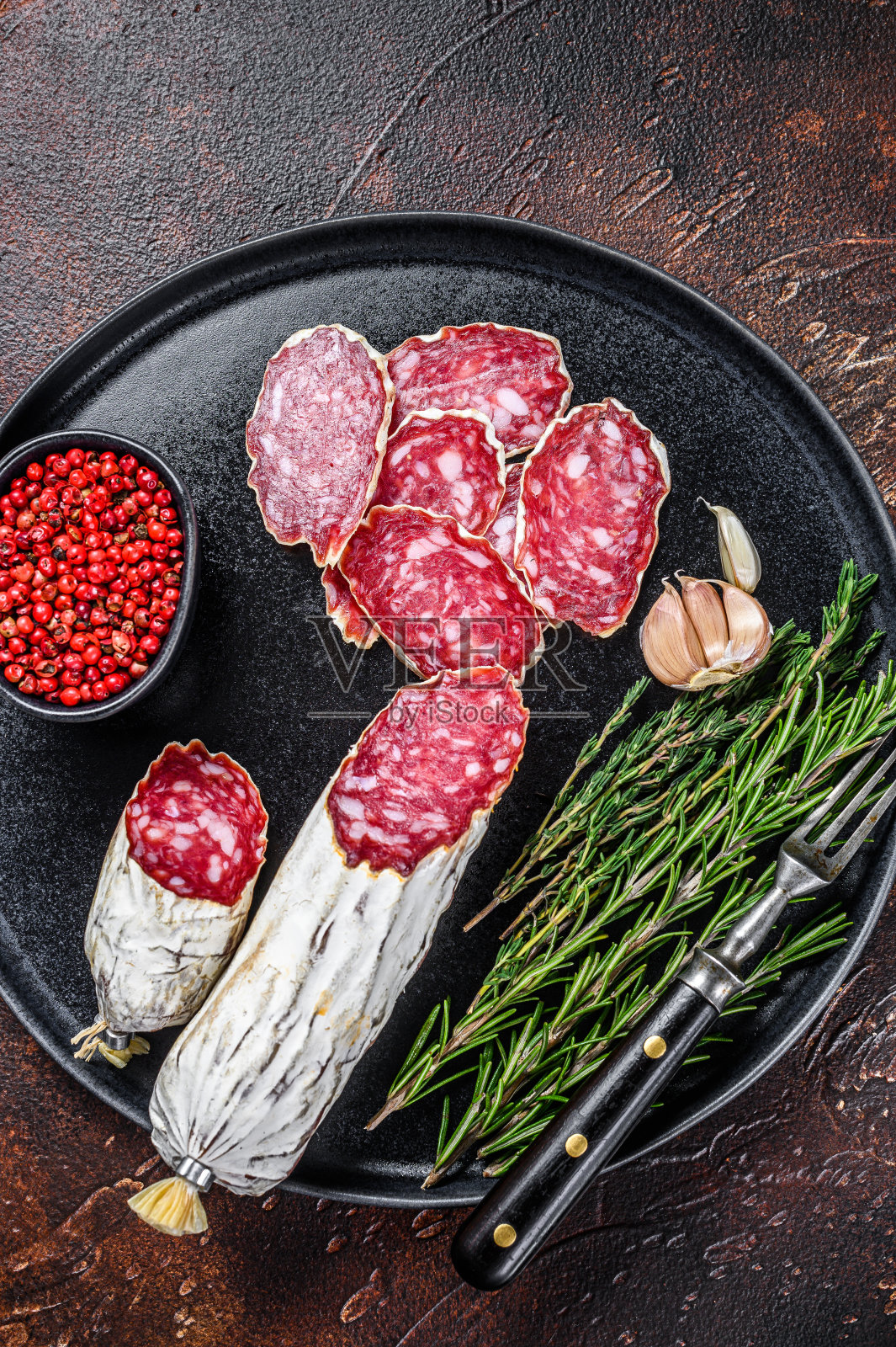 意大利腊肠切片,配上迷迭香和百里香。黑暗的背景。俯视图照片摄影图片
