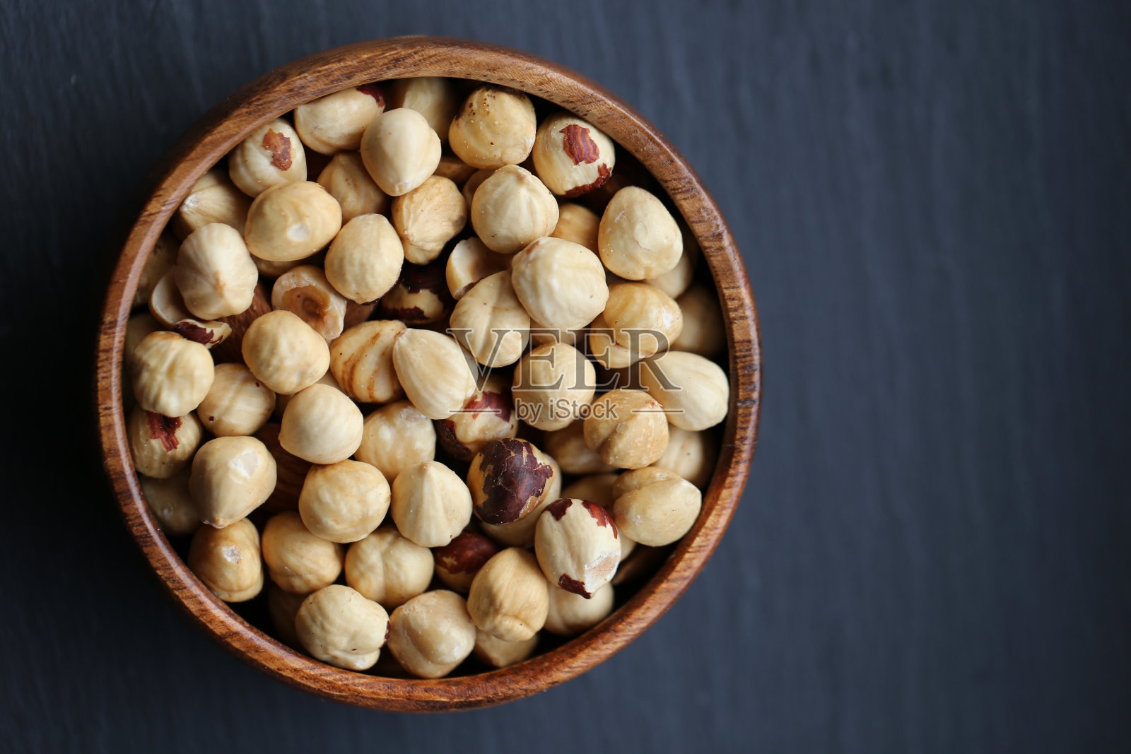 榛子在一个木制的圆杯里剥皮,背景是破旧的黑色木板。前视图。健康食品和零食。照片摄影图片