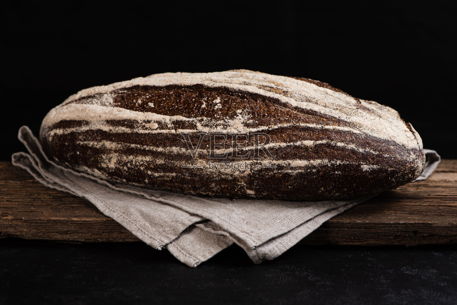 在木板上新鲜烘焙的自制酸面团黑麦面包。农家面包在发酵的特写。低调。照片摄影图片