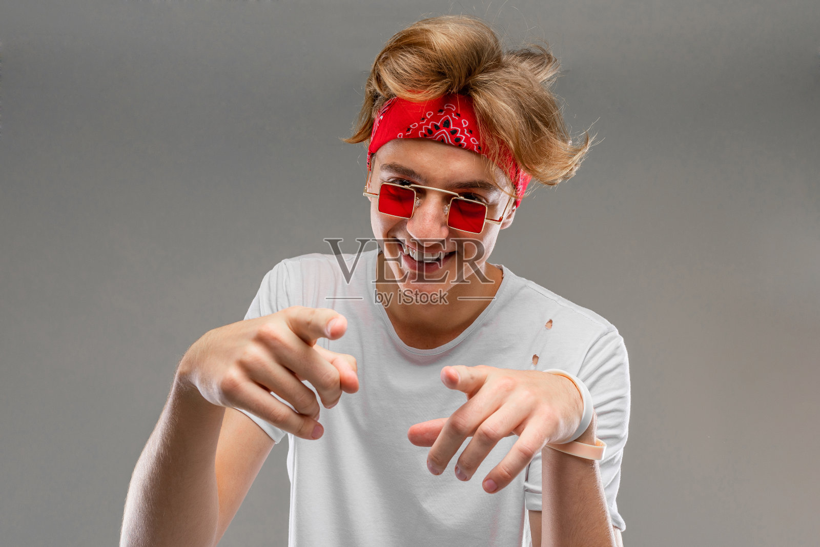 一个穿着白色t恤,戴着眼镜,头上戴着大手帕的自信的时尚男士被孤立在灰色的背景中照片摄影图片