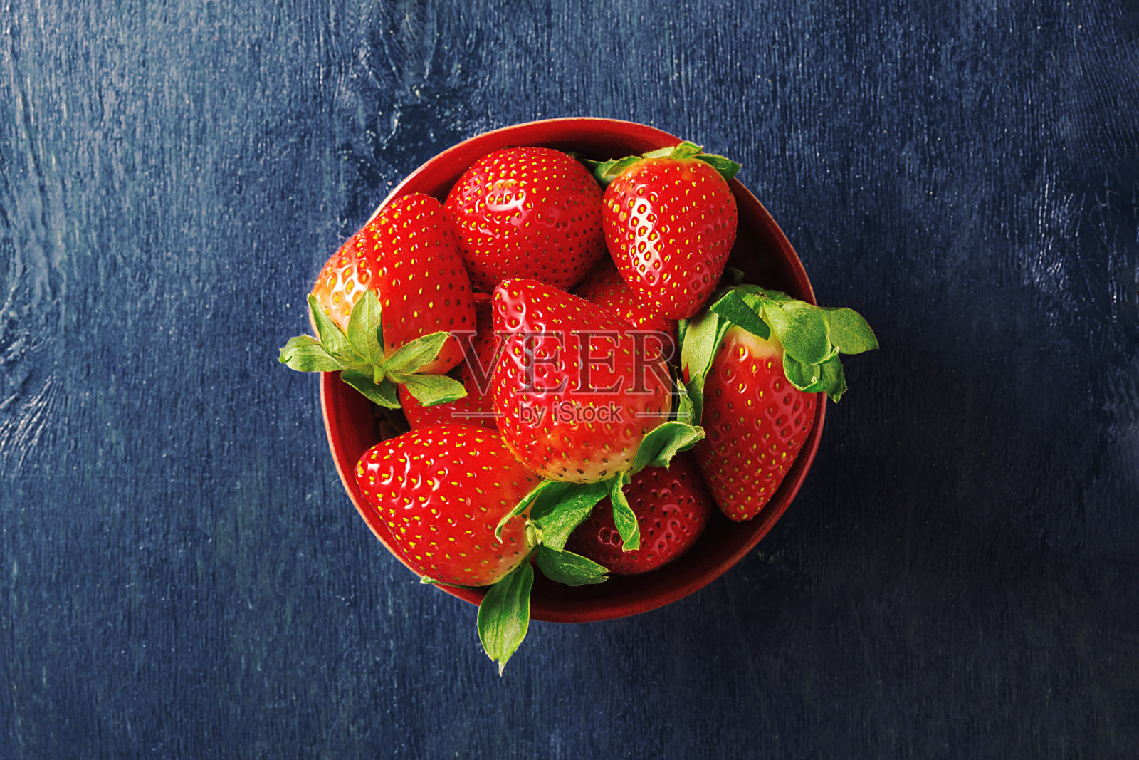 深蓝色背景上的一碗多汁的草莓。前视图。照片摄影图片