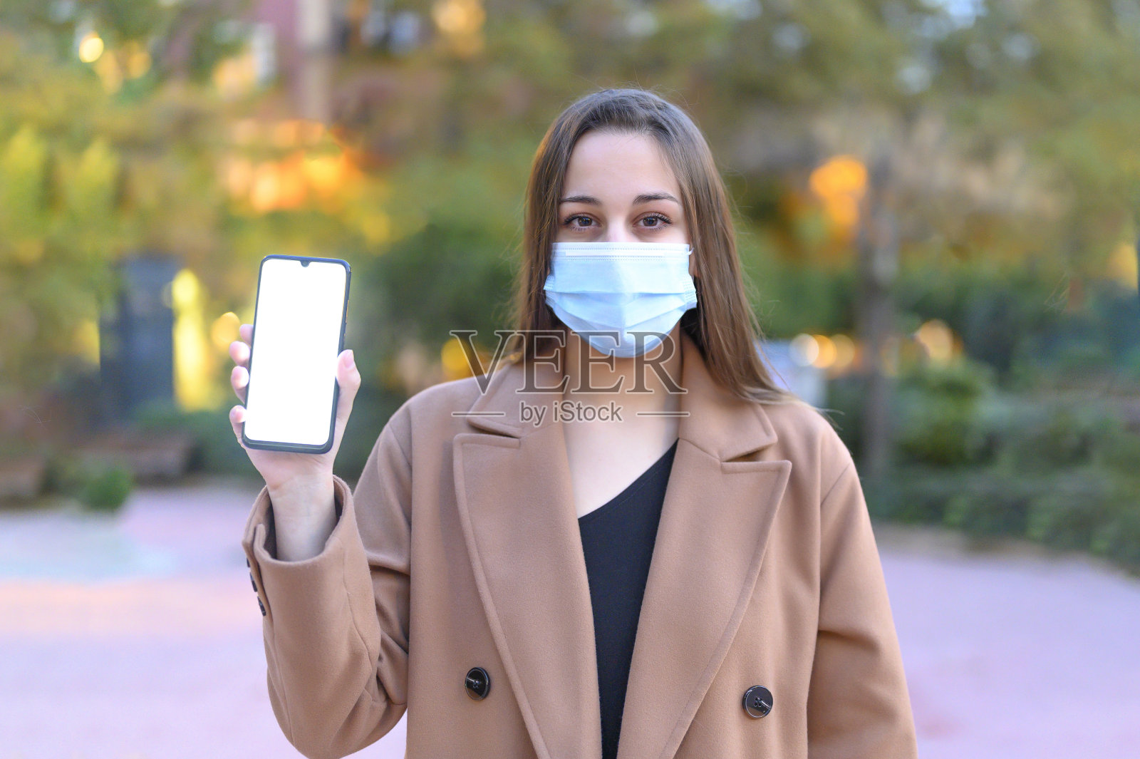 戴着防护面具的严肃女人在街上展示着空白的智能手机屏幕照片摄影图片