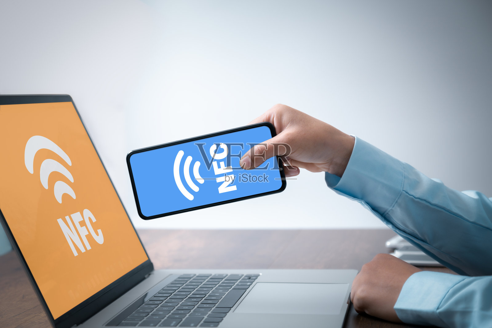 近场通信(NFC)手拿着NFC标记的手机靠近笔记本电脑进行配对。照片摄影图片