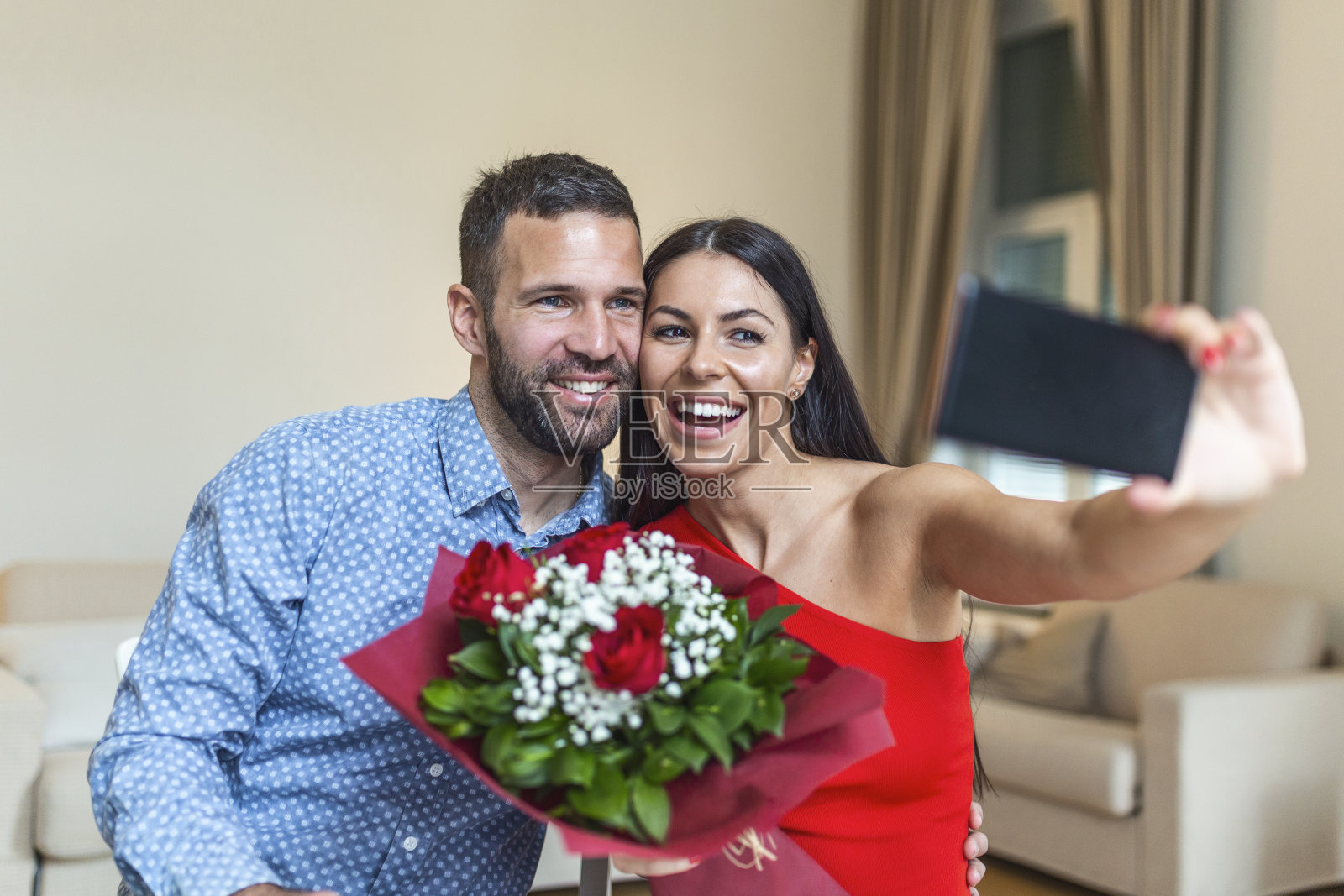 快乐的年轻夫妇在家中度过浪漫时光,用鲜花自拍,庆祝情人节照片摄影图片