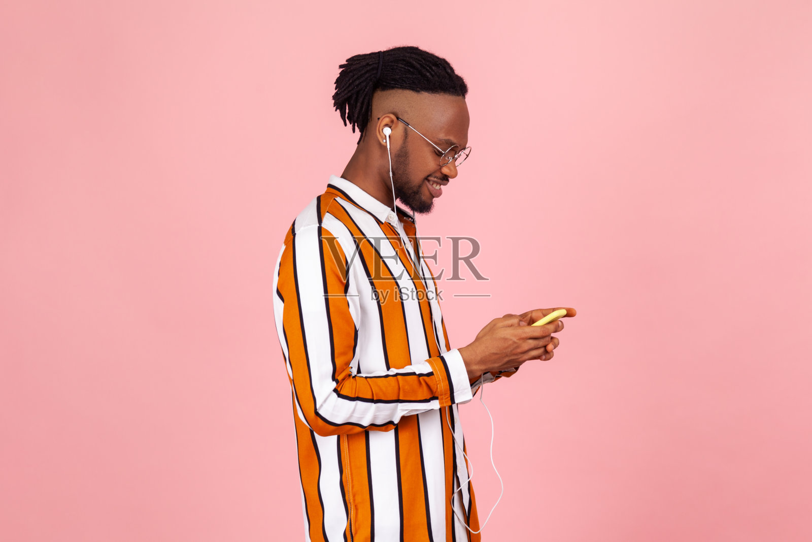 一名穿着条纹衬衫戴着耳机、梳着雷鬼辫的美国黑人在一边听着音乐一边聊天照片摄影图片