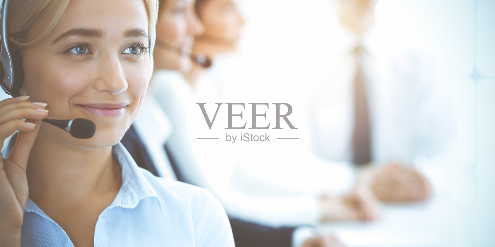 微笑着的女商人戴着耳机向客户咨询。一组不同的电话运营商在阳光办公室工作。呼叫中心和商务人士的概念照片摄影图片