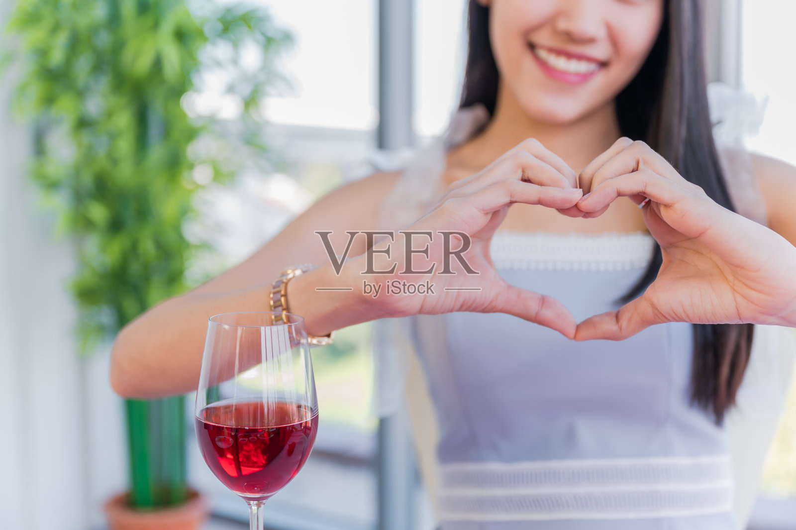 美丽的亚洲年轻女子坐和快乐的微笑与显示心形的手势由她的手照片摄影图片