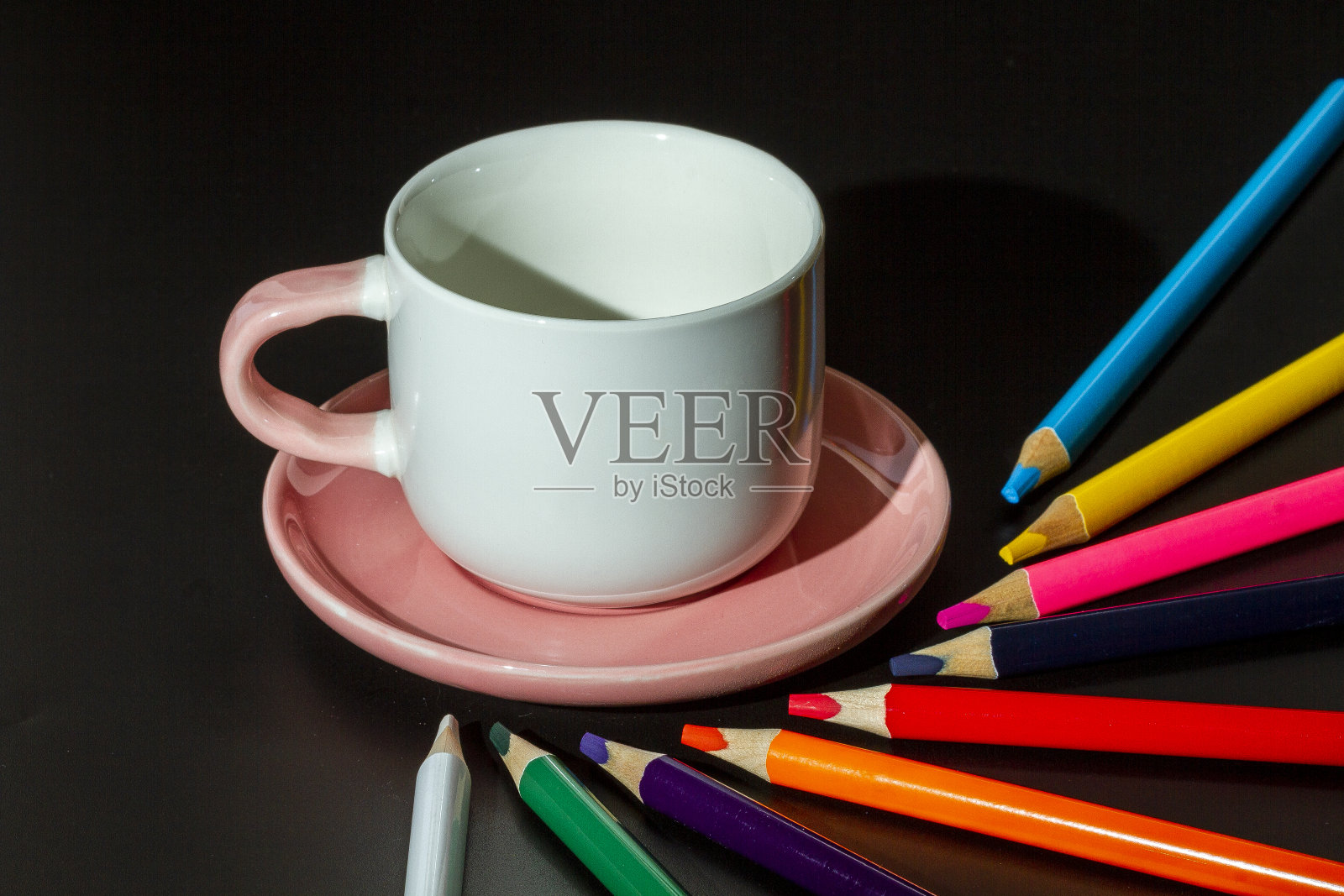 带有粉色茶托和彩色铅笔的白色杯子照片摄影图片