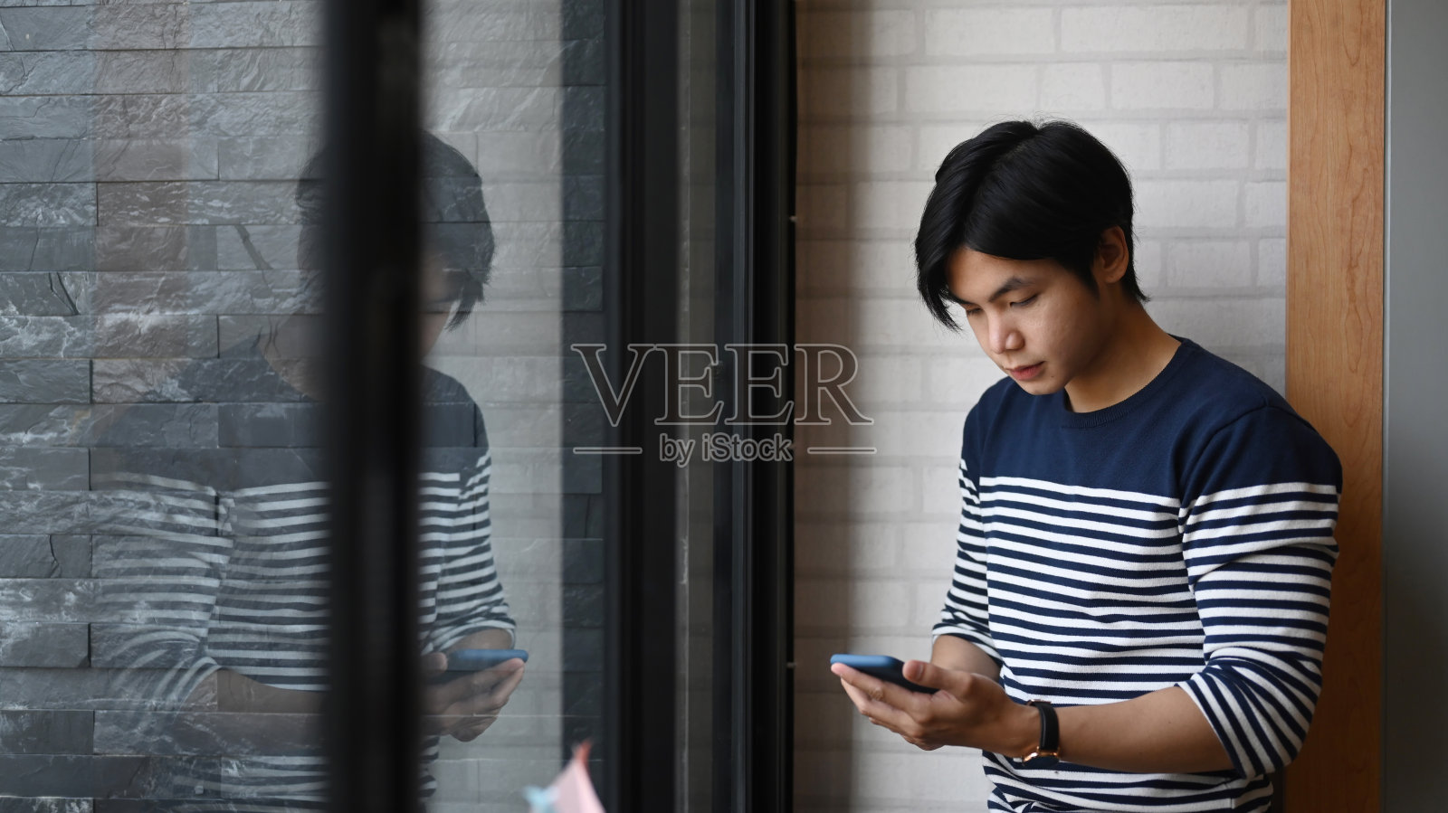 自信的年轻商人站在办公室窗户附近使用手机。照片摄影图片