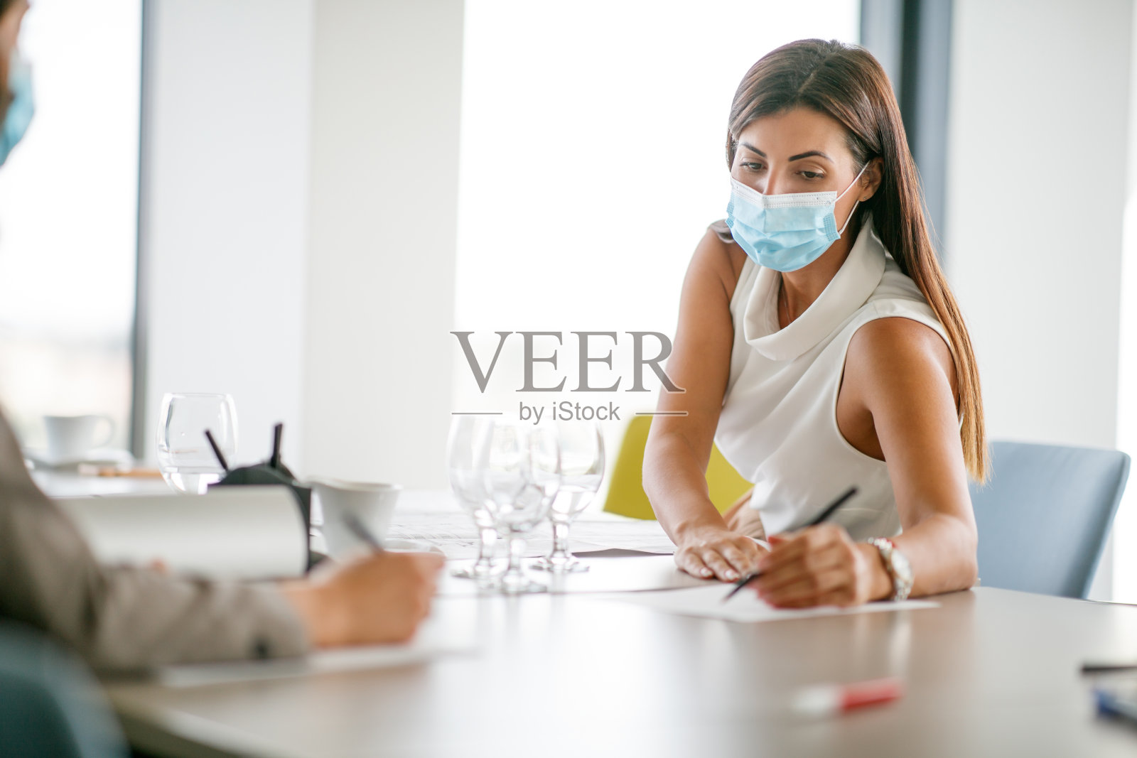 年轻的女商人戴着防护面罩与同事讨论业务照片摄影图片