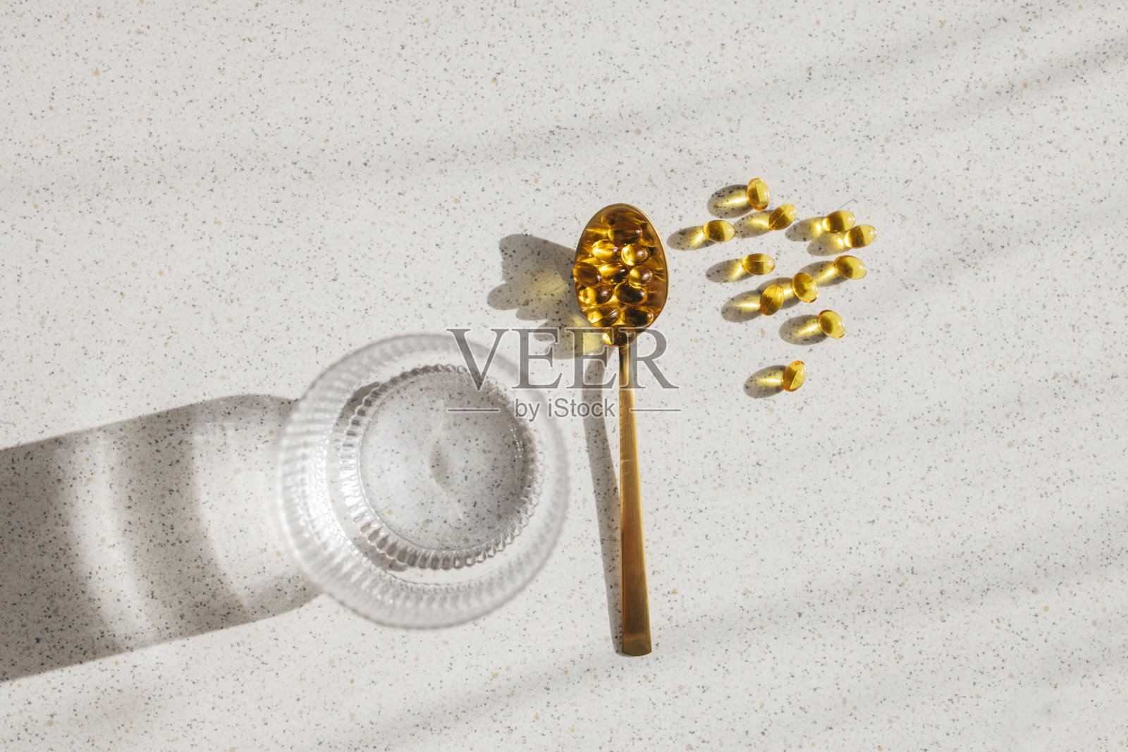 维生素D药丸在茶匙中,放在桌子上,旁边是一杯水(高角度照片)照片摄影图片