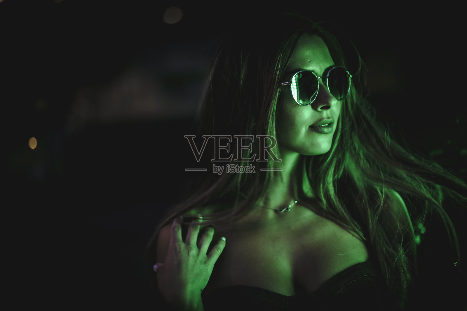 白人黑发女孩戴着太阳镜看着浅绿色的led灯。夜晚城市摄影照片摄影图片