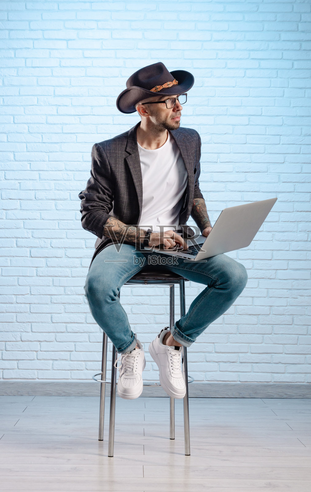 一名穿着夹克、头戴牛仔帽、手拿笔记本电脑的时尚男子在演播室摆姿势照片摄影图片