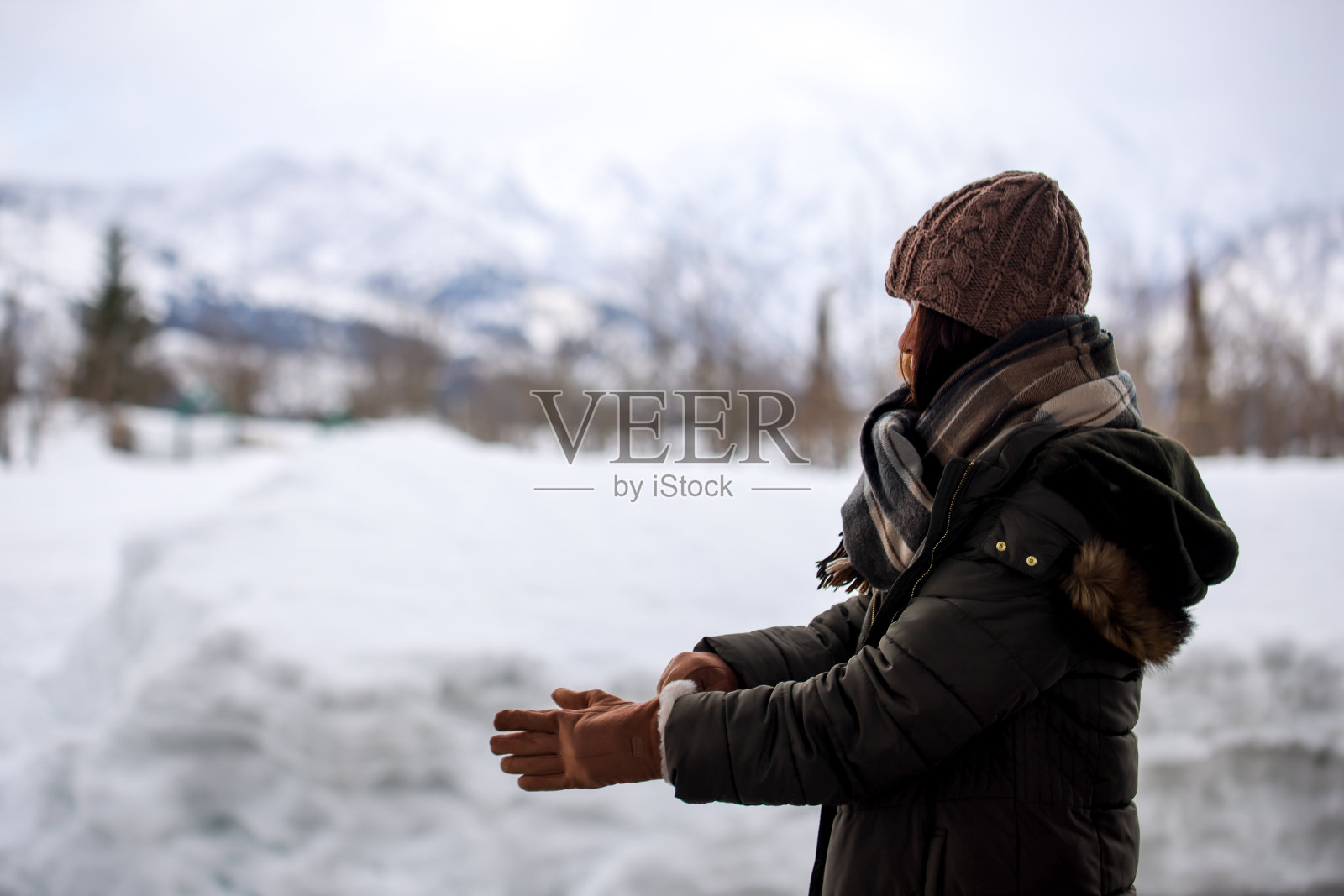 美丽的年轻女子戴着她的手套在白雪覆盖的公园照片摄影图片