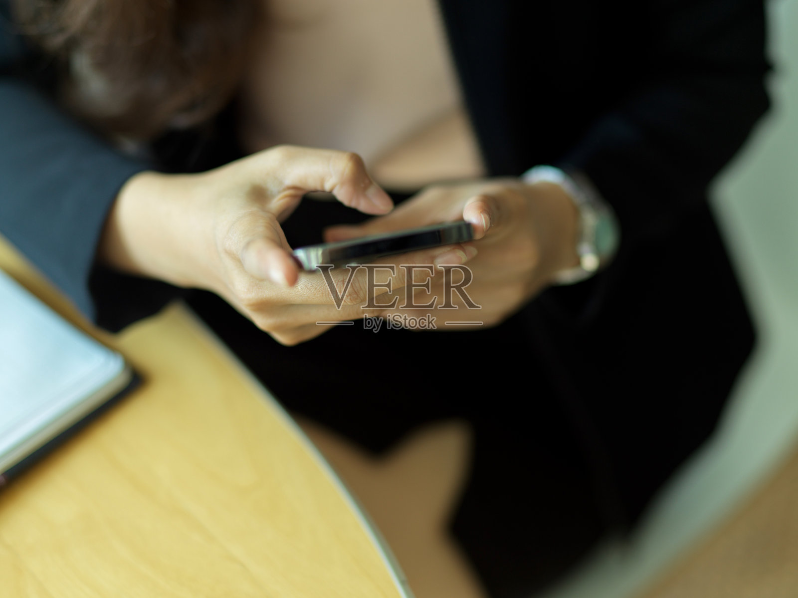 在办公室工作时,穿着黑色西装的女商人用智能手机发短信照片摄影图片