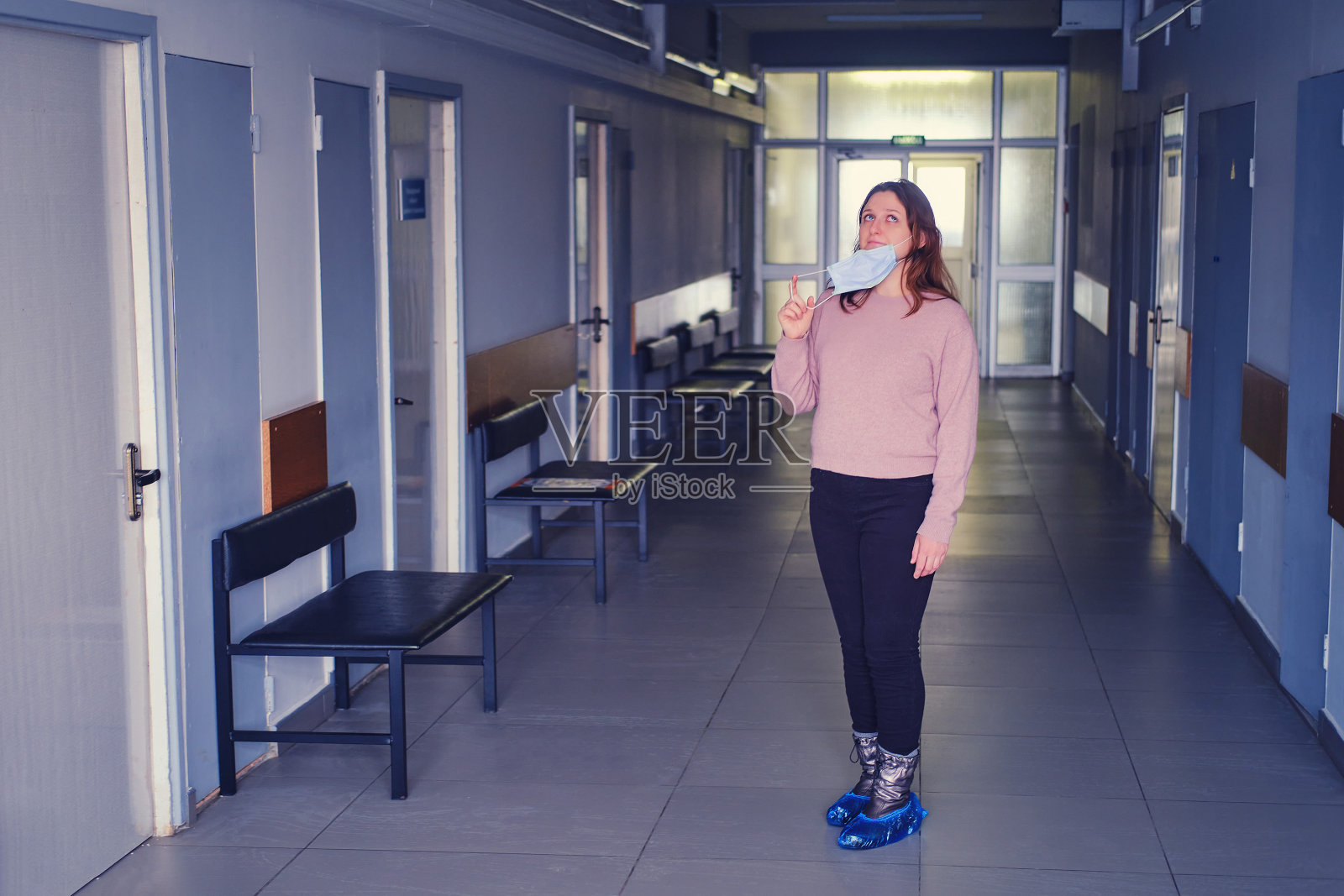 在空荡荡的医院走廊里,一名妇女摘下了脸上的口罩。结束冠状病毒大流行的挑战照片摄影图片