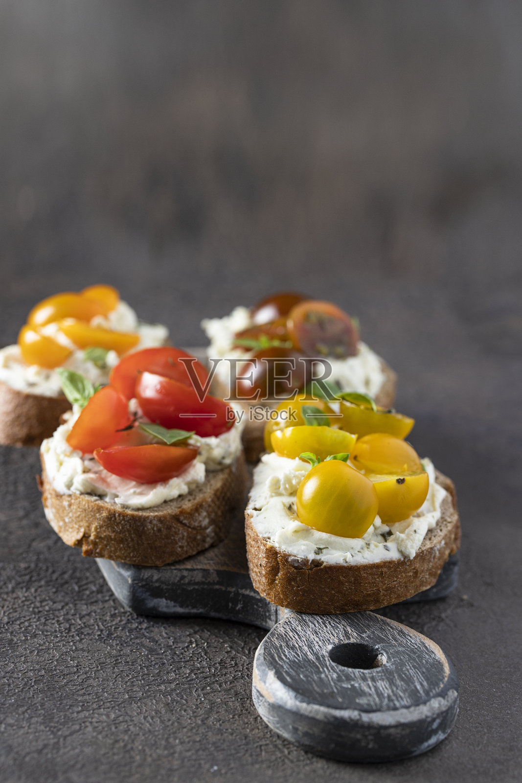 自制的意式烤面包,配以奶油芝士和不同的番茄樱桃装饰新鲜的罗勒叶。美味的开胃菜照片摄影图片