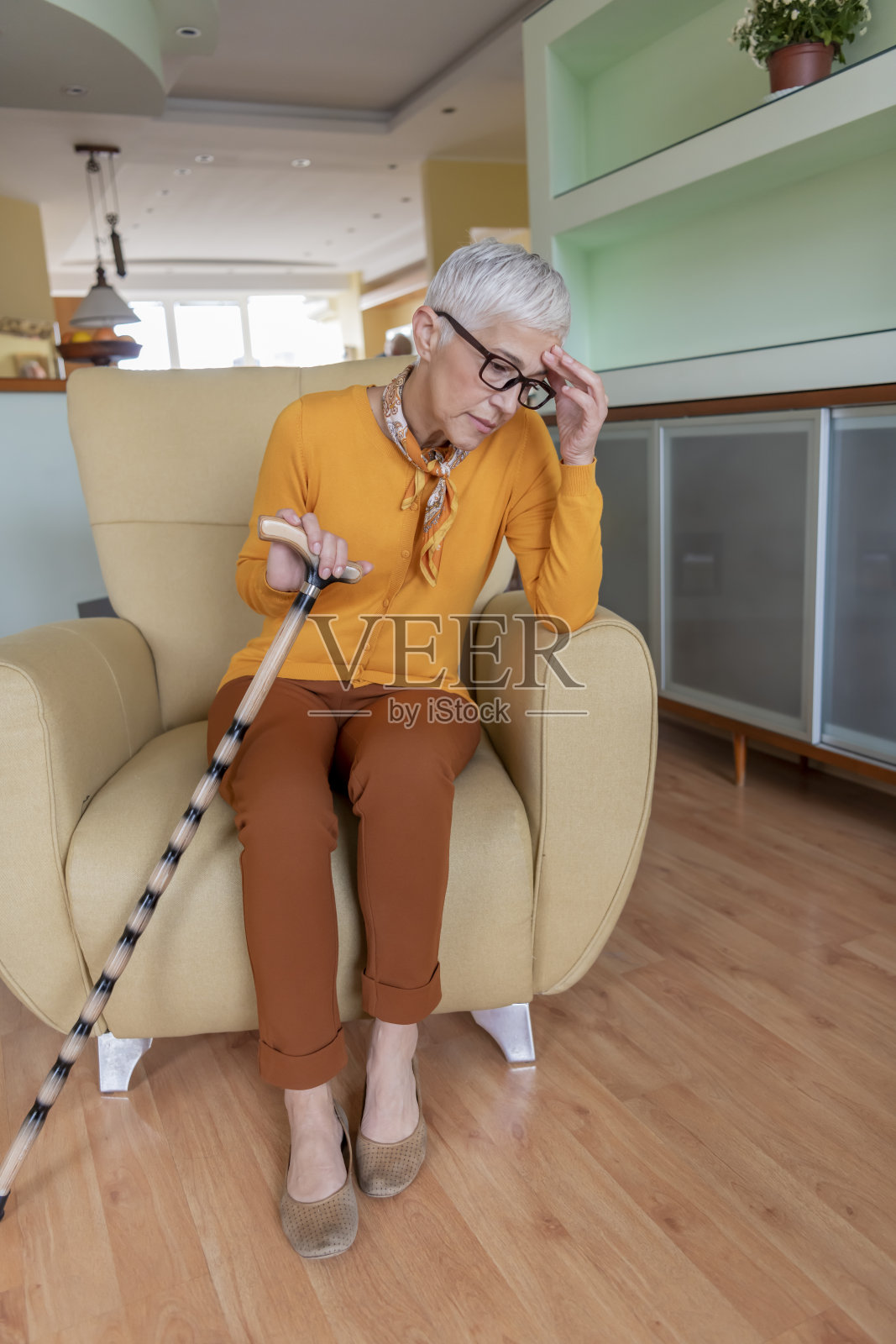 孤独的老年妇女坐在家里的沙发上,看起来很悲伤。照片摄影图片